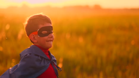 Der-Junge-Mit-Der-Maske-Und-Dem-Umhang-Eines-Superhelden-Bei-Sonnenuntergang-Auf-Einem-Feld.